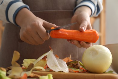 Photo of Woman peeling fresh carrot with knife at table indoors, closeup