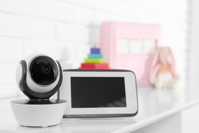 Photo of Baby monitor with camera on table near white brick wall. Video nanny