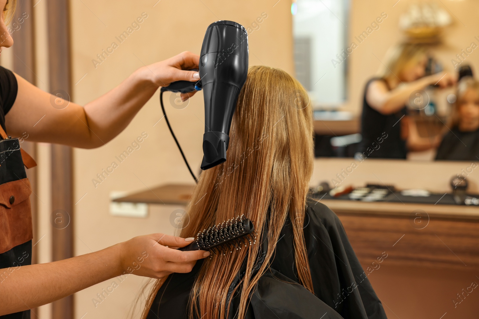 Photo of Professional hairdresser drying girl's hair in beauty salon, closeup