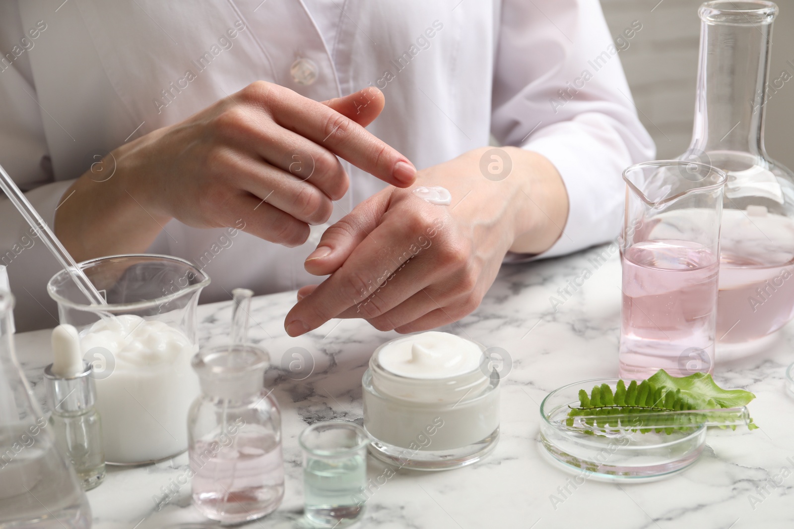 Photo of Scientist testing cosmetic product at white marble table in laboratory, closeup