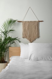 Stylish macrame hanging on white wall in bedroom