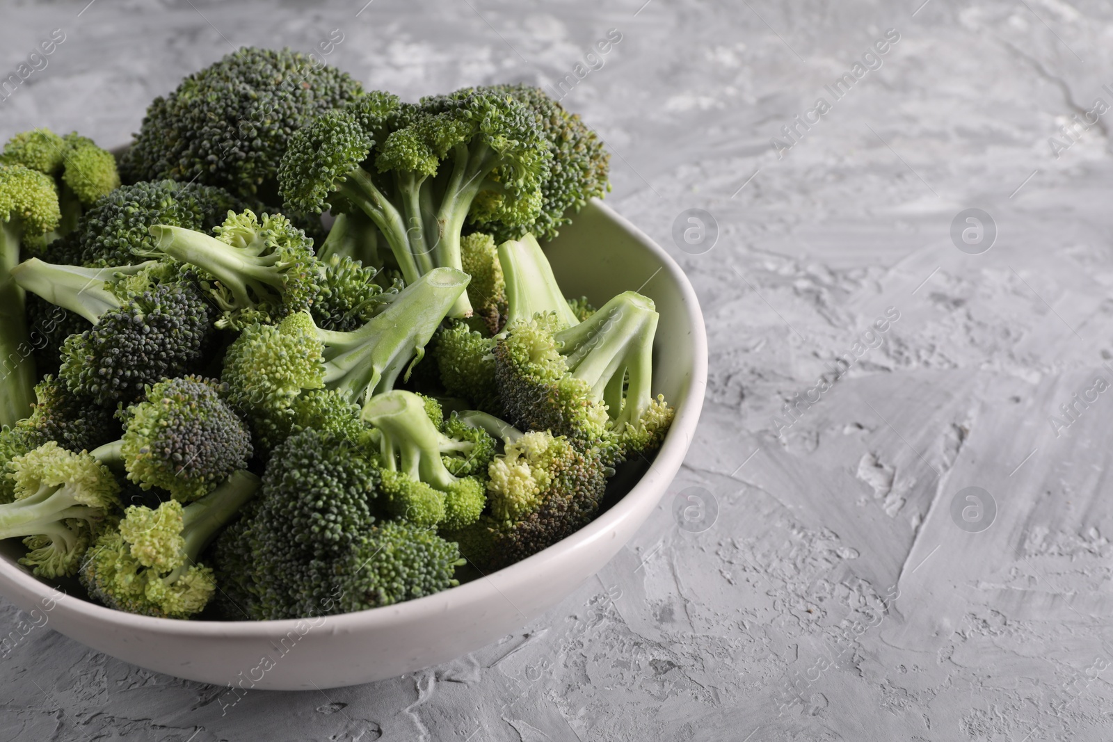 Photo of Bowl of fresh raw broccoli on grey textured table, closeup. Space for text