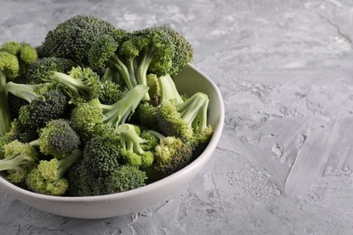 Bowl of fresh raw broccoli on grey textured table, closeup. Space for text