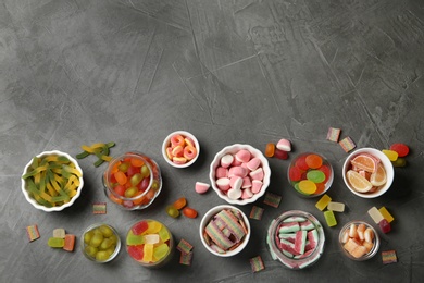 Photo of Flat lay composition with bowls of different jelly candies on black stone background. Space for text