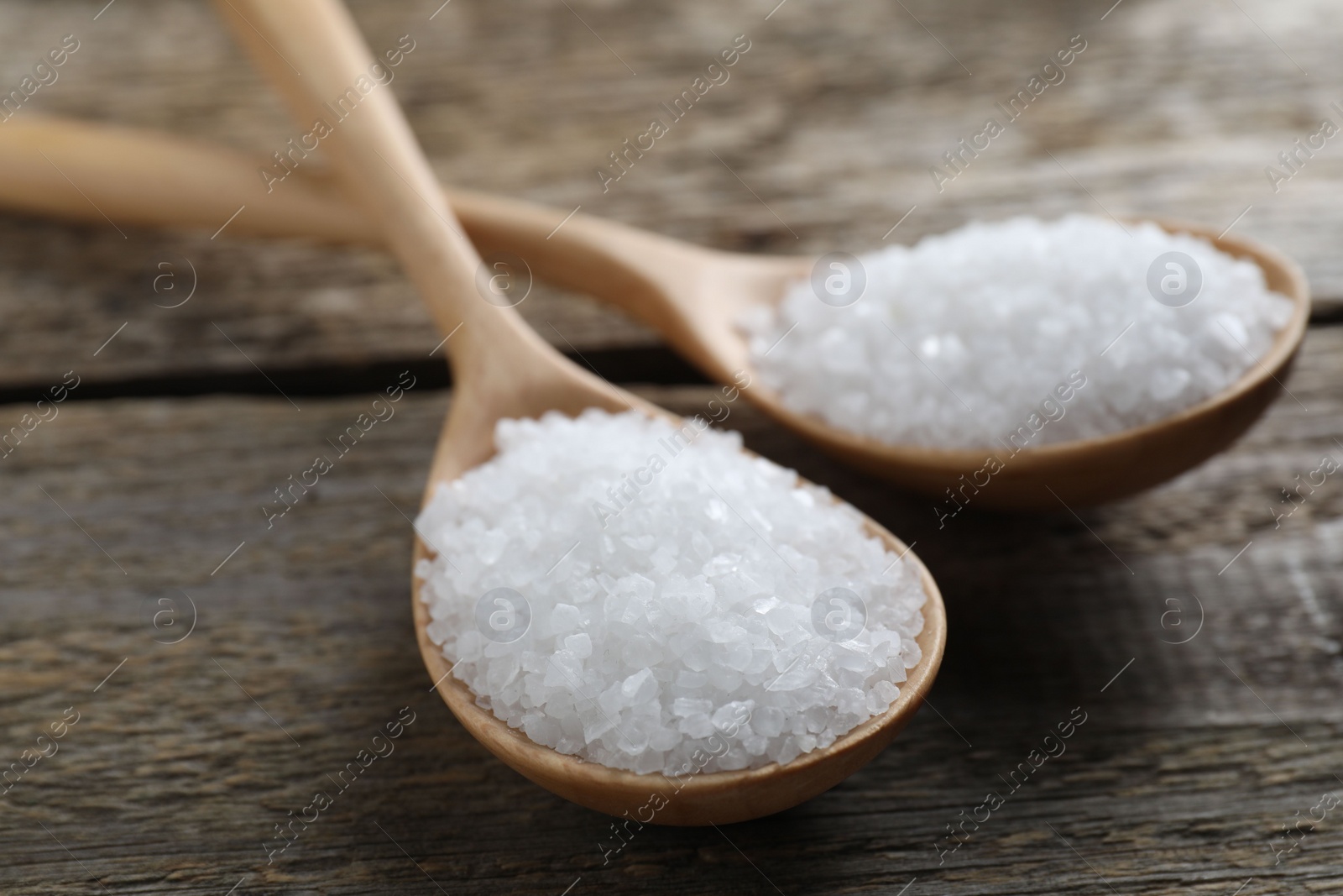 Photo of Organic salt in spoons on wooden table, closeup