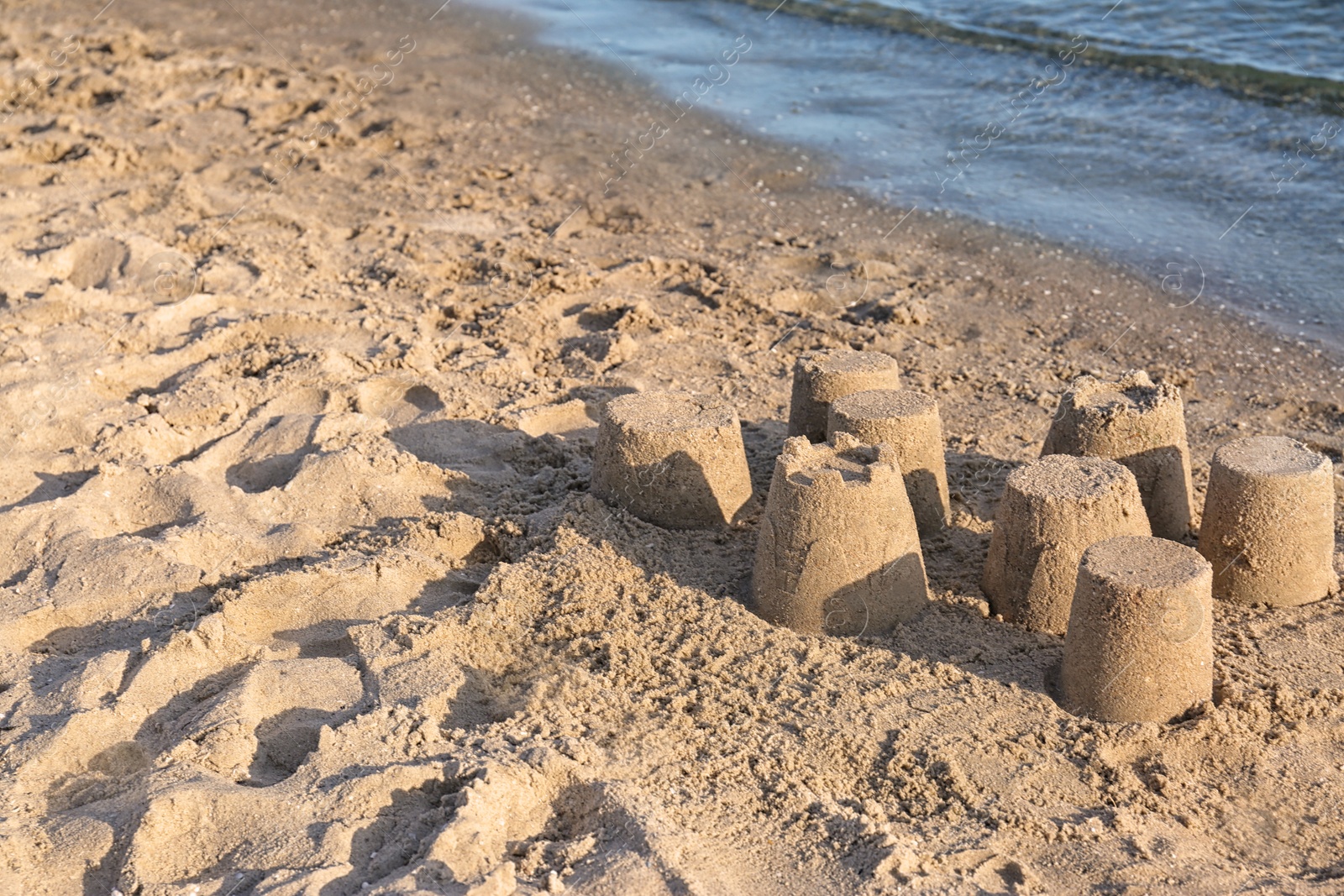 Photo of View of beach with little sand figures near sea on sunny summer day. Space for text