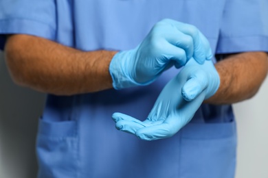 Photo of Doctor putting on medical gloves against light grey background, closeup