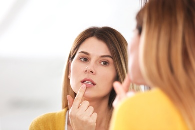 Photo of Woman applying cold sore cream on lips in front of mirror