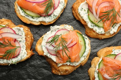 Photo of Tasty canapes with salmon, cucumber, radish and cream cheese on slate board, top view