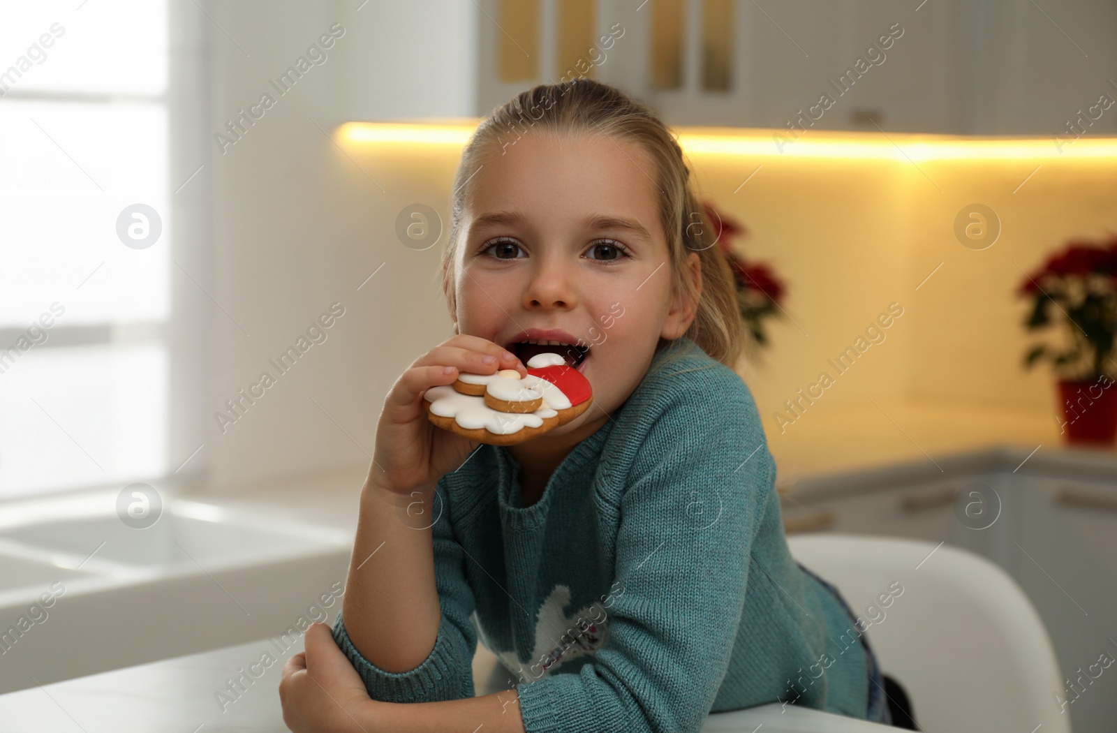 Photo of Cute little girl with Christmas gingerbread cookie at table indoors