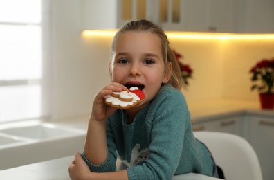 Cute little girl with Christmas gingerbread cookie at table indoors