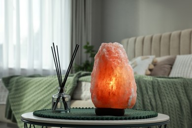 Beautiful Himalayan salt lamp and air reed freshener on table in bedroom
