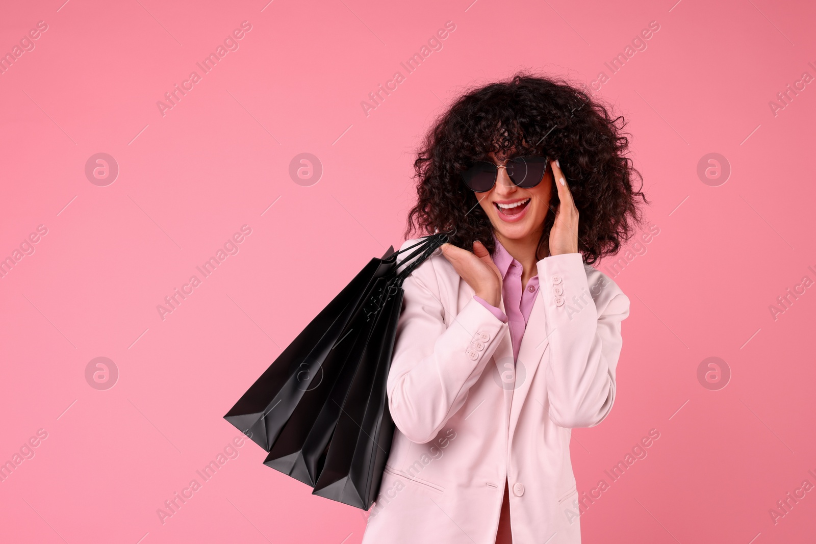 Photo of Happy young woman with shopping bags and stylish sunglasses on pink background. Space for text