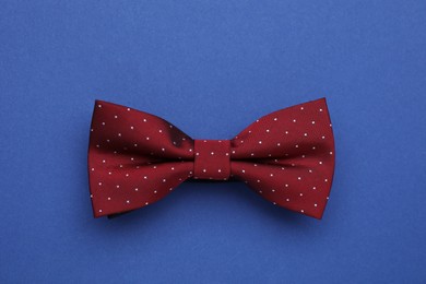 Stylish burgundy bow tie with polka dot pattern on blue background, top view