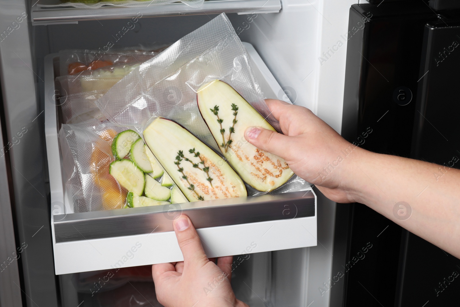 Photo of Woman putting vacuum bag with eggplant into fridge, closeup. Food storage