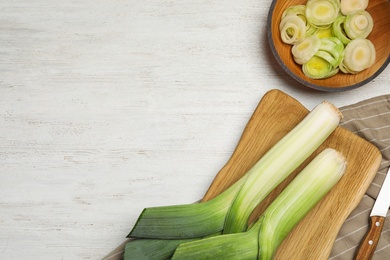 Photo of Flat lay composition with fresh raw leeks on white wooden table, space for text. Ripe onion