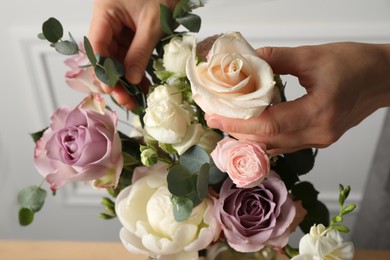 Photo of Florist creating beautiful bouquet with roses indoors, closeup