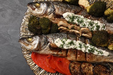 Plate with delicious sea bass fish and ingredients on dark grey table, top view