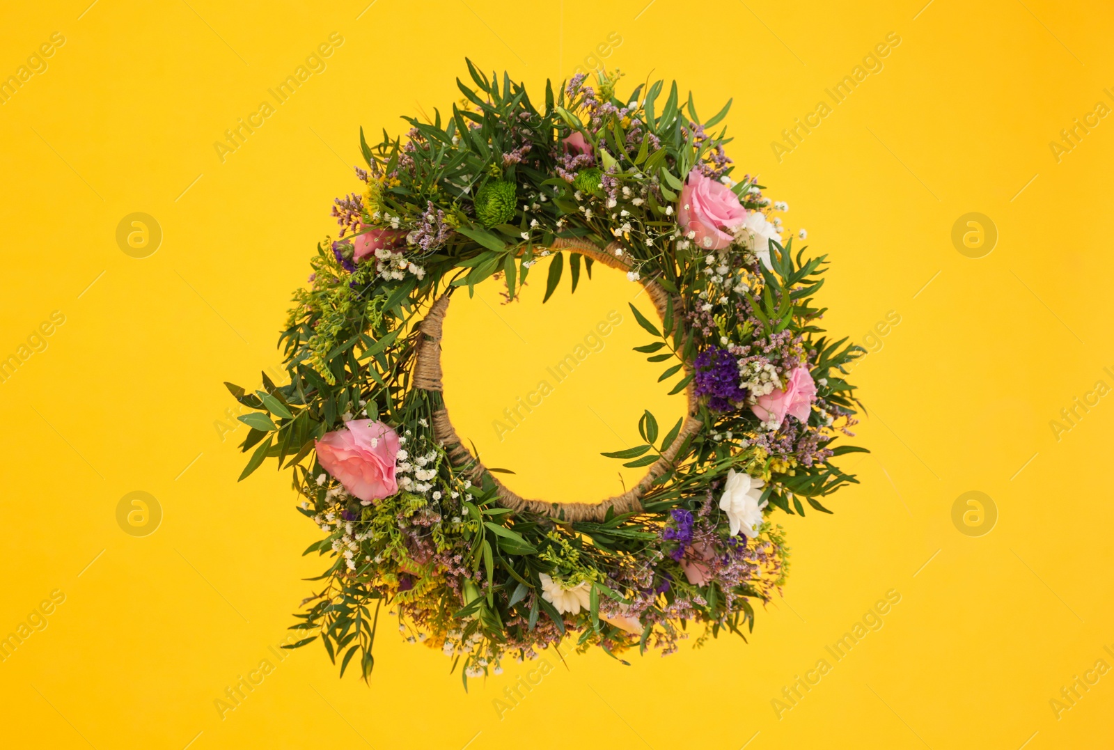 Photo of Wreath made of beautiful flowers hanging on yellow background
