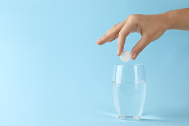 Photo of Woman putting tablet into glass of water on light blue background, space for text