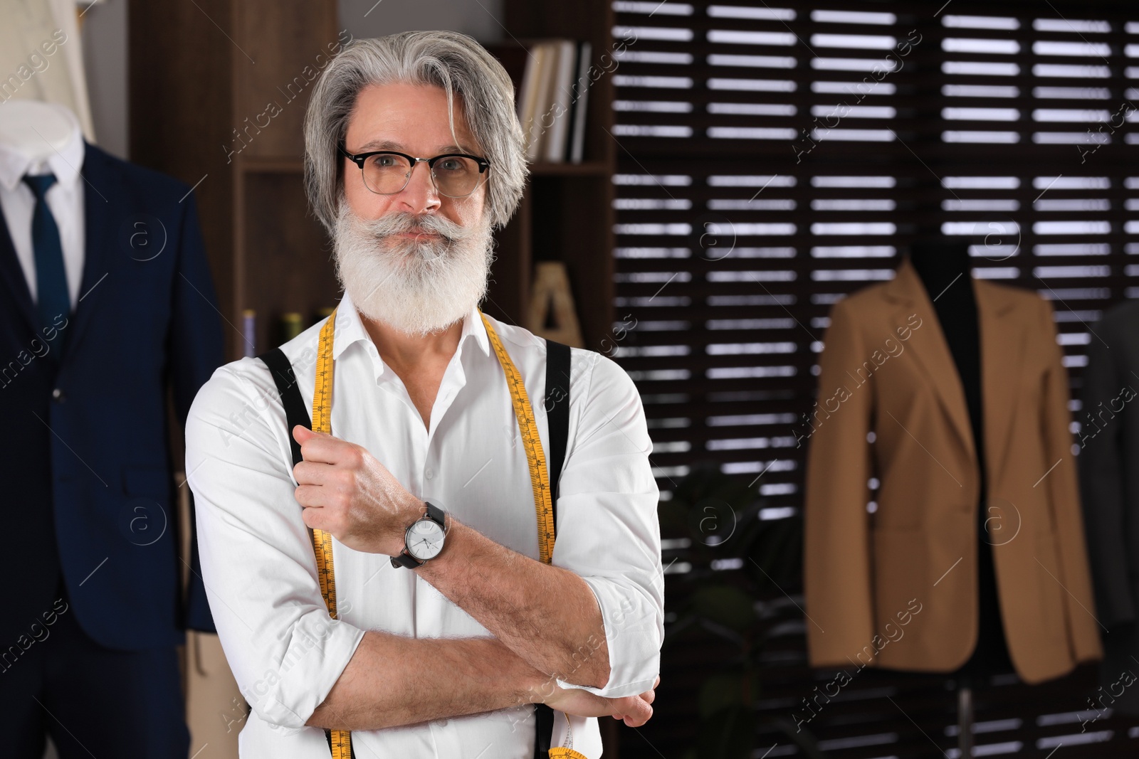 Photo of Professional tailor with measuring tape in workshop, space for text