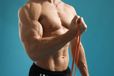 Muscular man exercising with elastic resistance band on light blue background, closeup