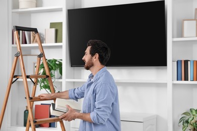 Man with books near wooden folding ladder at home