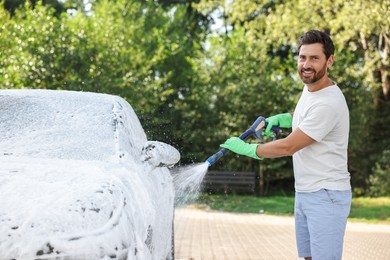 Photo of Happy man covering automobile with foam at outdoor car wash