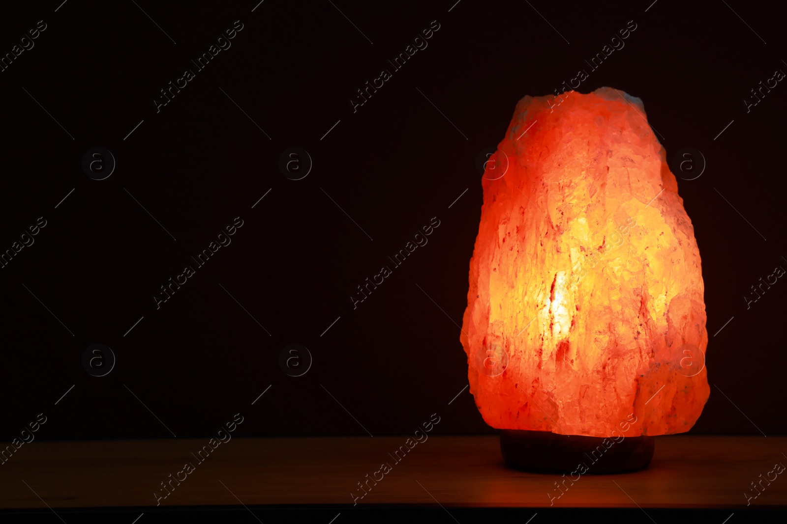 Photo of Himalayan salt lamp on wooden table against dark background, space for text