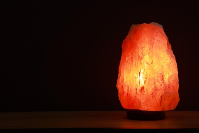 Photo of Himalayan salt lamp on wooden table against dark background, space for text