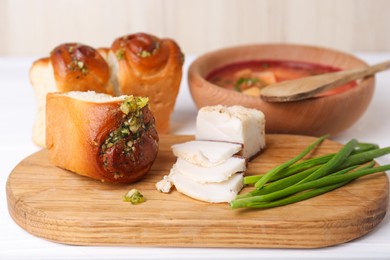Photo of Delicious pampushky (buns with garlic), green onions and salo served for borsch on white table, closeup. Traditional Ukrainian cuisine