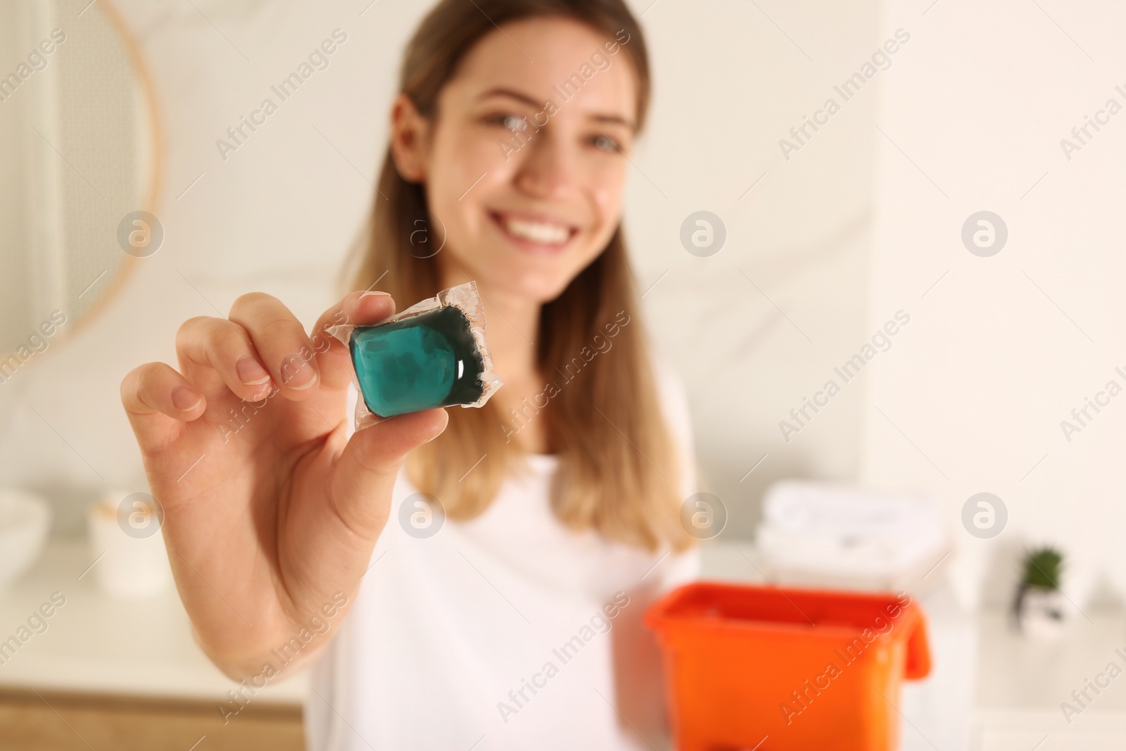 Photo of Happy woman holding laundry detergent capsule indoors, focus on hand