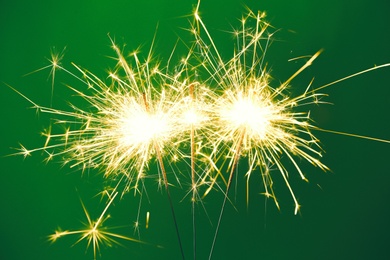 Photo of Bright burning sparklers on green background, closeup