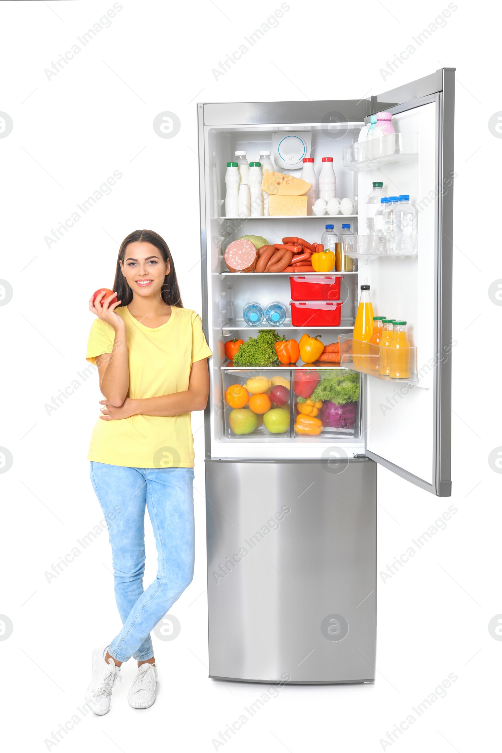 Photo of Young woman with apple near open refrigerator on white background