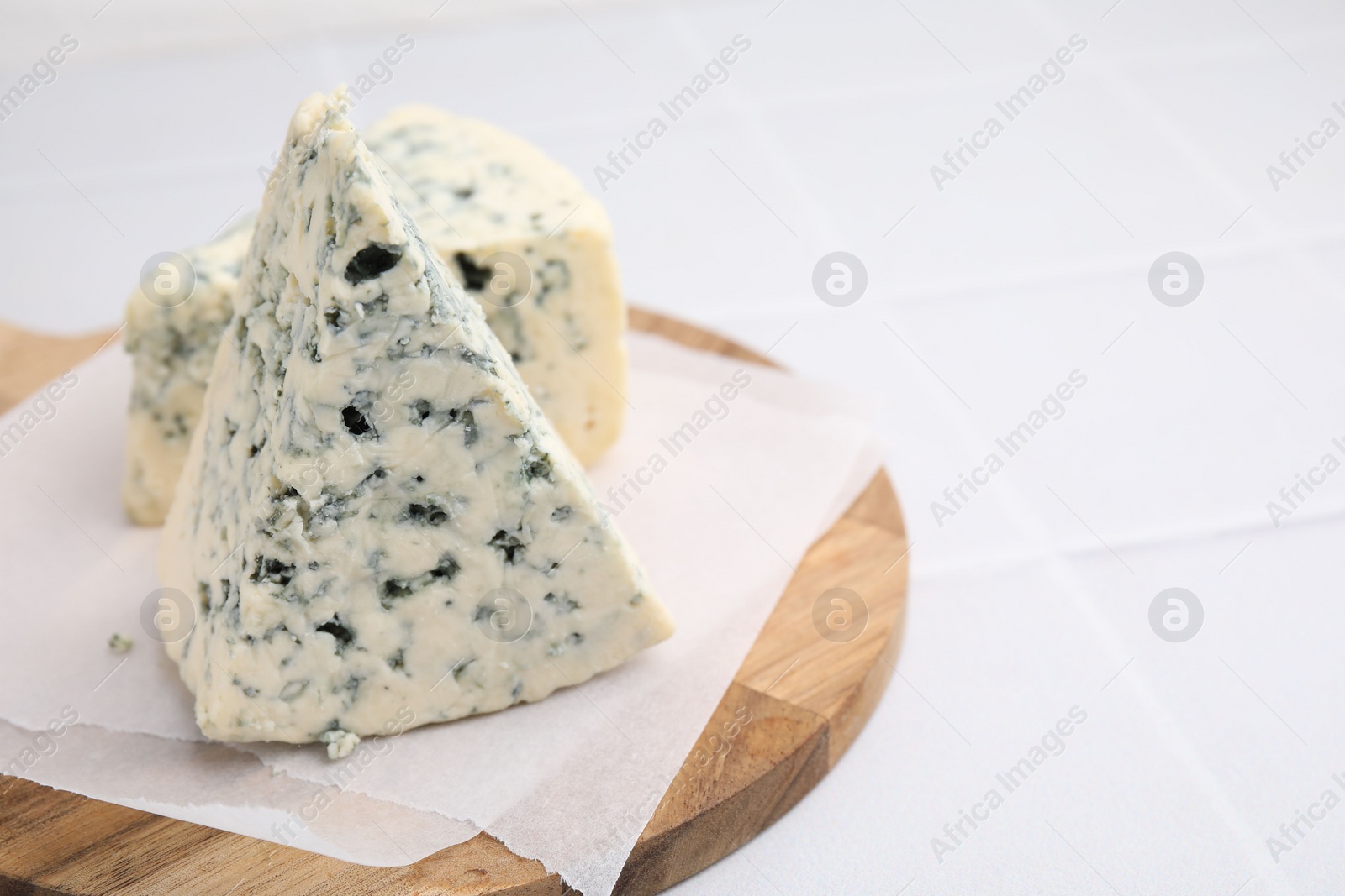 Photo of Wooden cutting board with blue cheese on white tiled table, closeup. Space for text