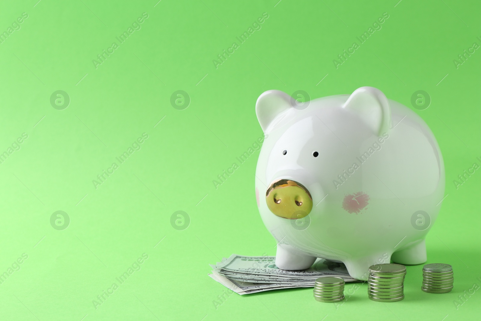 Photo of Financial savings. Piggy bank, dollar banknotes and stacked coins on green background, space for text