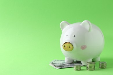 Photo of Financial savings. Piggy bank, dollar banknotes and stacked coins on green background, space for text