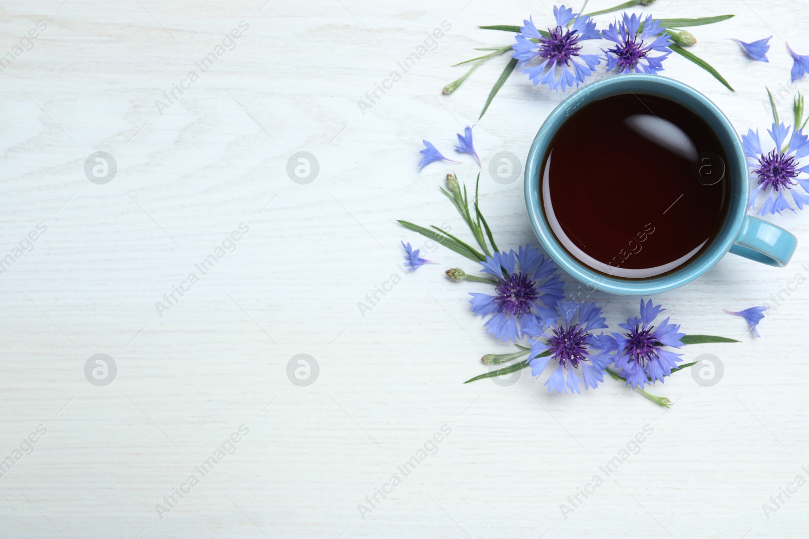 Photo of Cup of tea and cornflowers on white wooden table, flat lay. Space for text