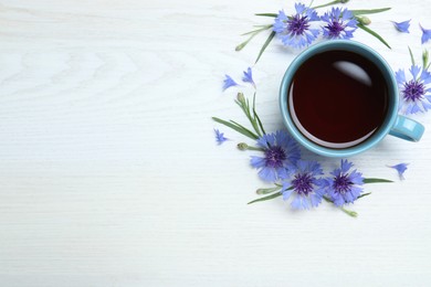 Cup of tea and cornflowers on white wooden table, flat lay. Space for text