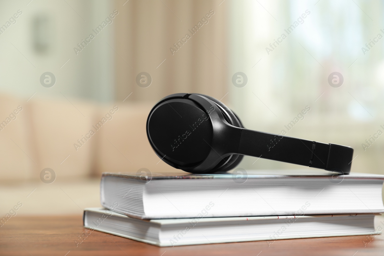 Photo of Modern wireless headphones and books on wooden table indoors