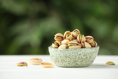 Photo of Tasty pistachios in bowl on white table against blurred background. Space for text