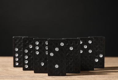 Photo of Domino tiles on wooden table against black background. Space for text