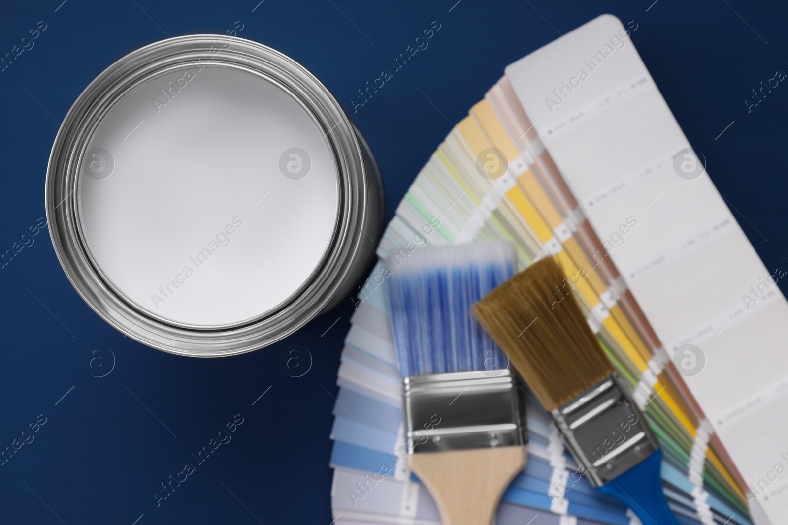 Photo of Can of white paint, brushes and palette on blue wooden table, flat lay