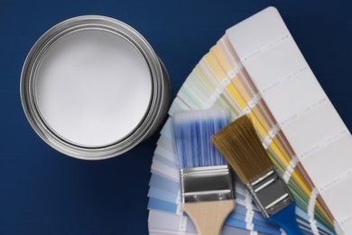 Photo of Can of white paint, brushes and palette on blue wooden table, flat lay