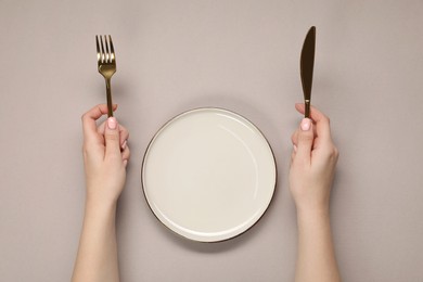 Photo of Woman holding fork and knife near empty plate at beige table, top view