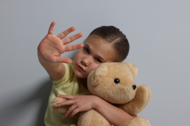Photo of Child abuse. Girl with toy making stop gesture near grey wall, selective focus