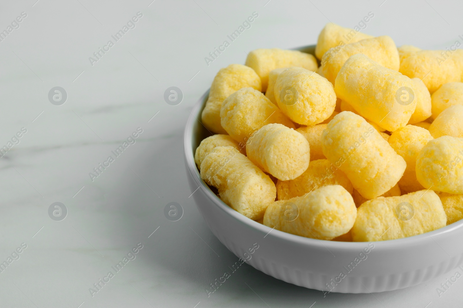 Photo of Bowl of delicious crispy corn sticks on white marble table. Space for text