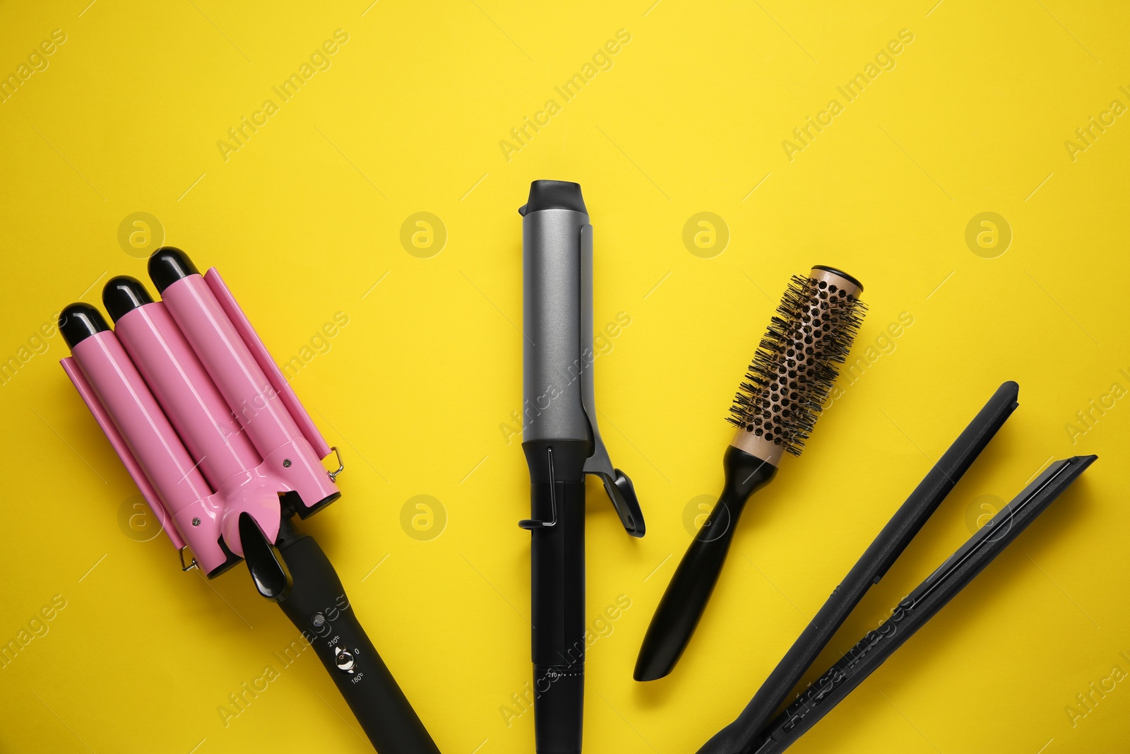 Photo of Different curling irons, hair straightener and round brush on yellow background, flat lay