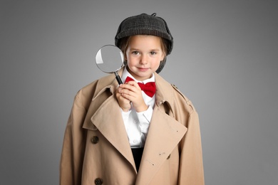 Cute little child in hat with magnifying glass playing detective on grey background