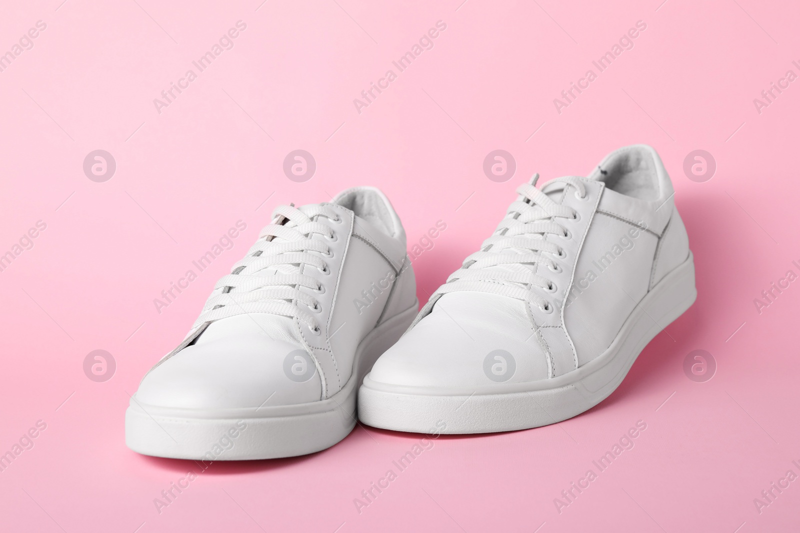 Photo of Pair of stylish white sneakers on pink background